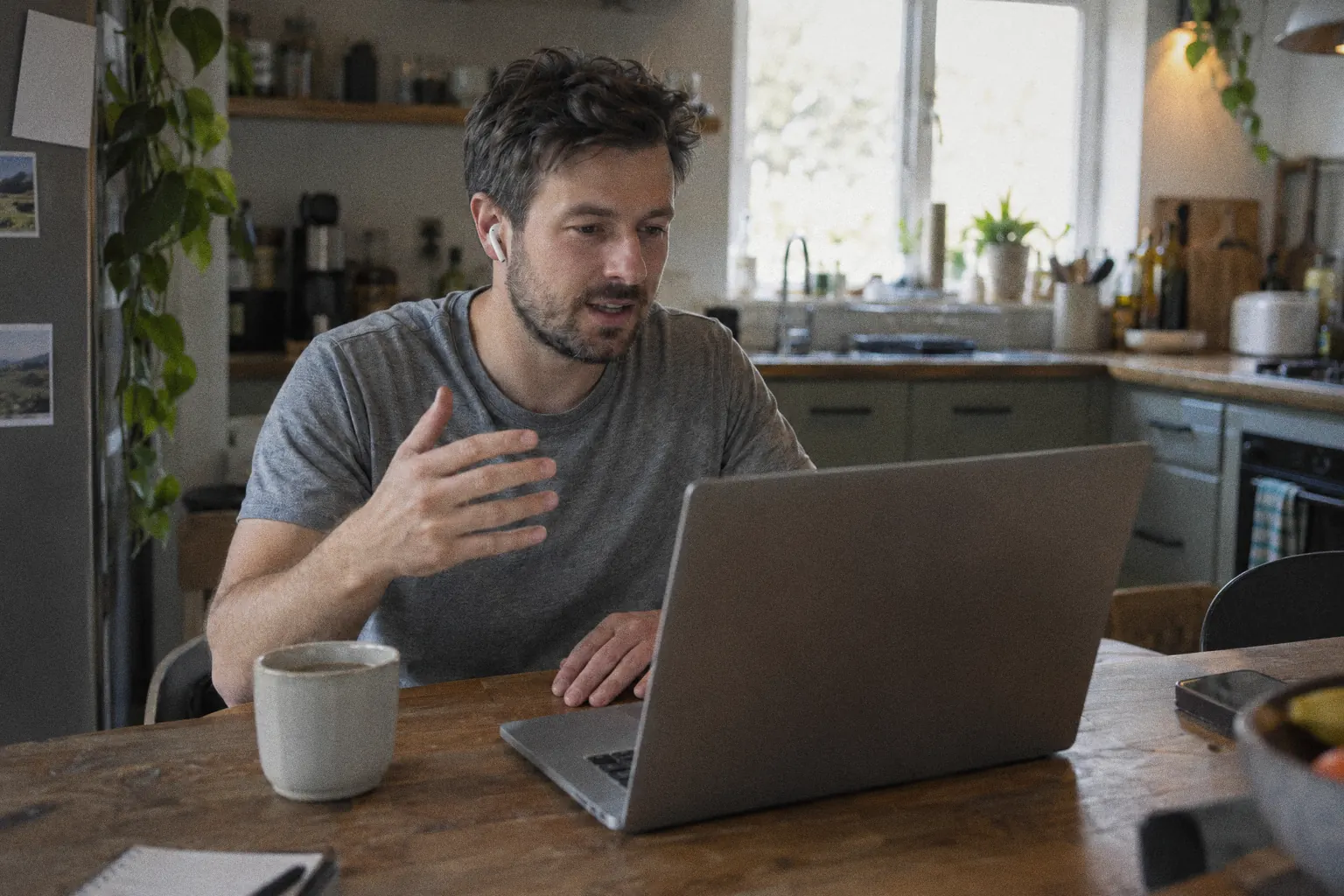 A founder on a video call at a kitchen table, laptop screen turned away from the camera.